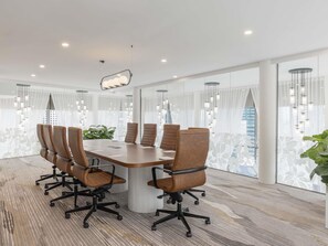 Un salón de conferencias con una mesa larga, seis sillas y ventanas grandes con cortinas.