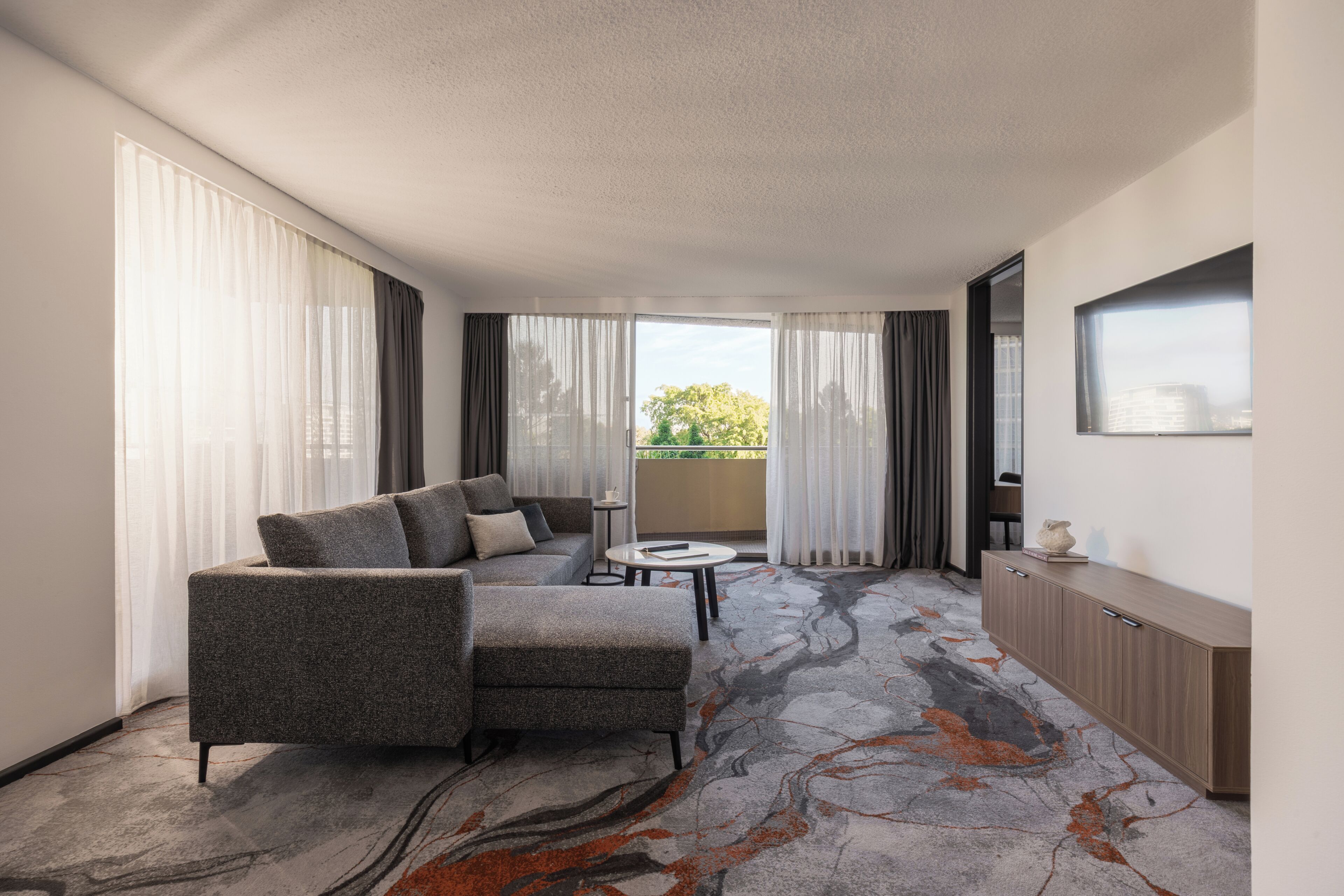 A modern hotel room with a grey sofa, a small round table, and a cabinet.