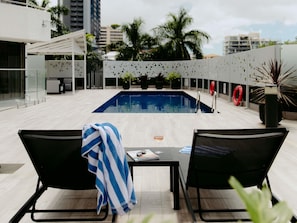 A rooftop pool area with two lounge chairs, a table, and a view of the cityscape. - Mercure Brisbane Spring Hill (Spring Hill)