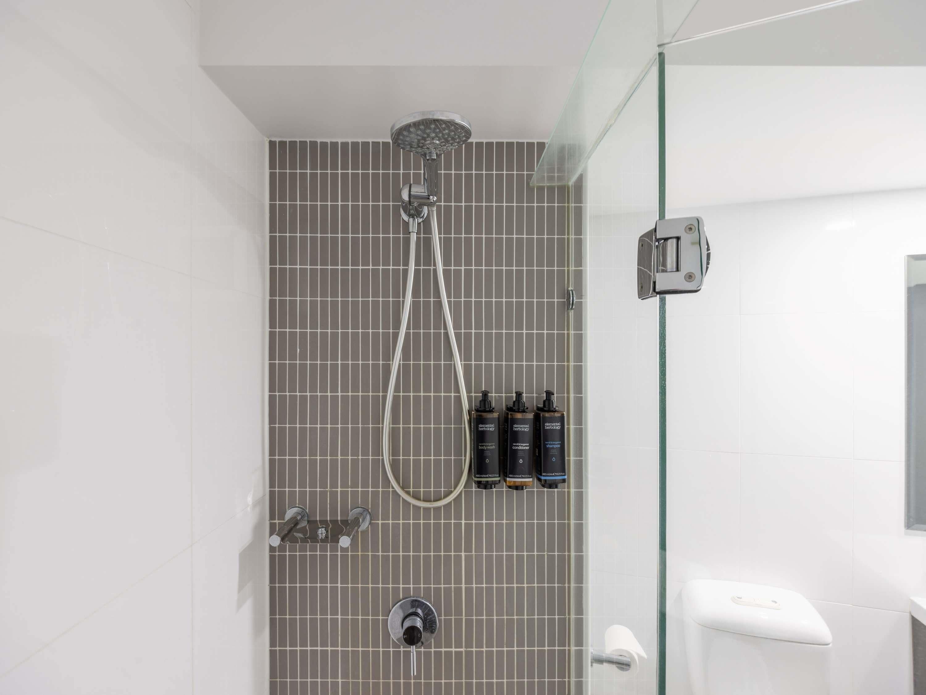 A modern shower with a handheld showerhead, a glass-enclosed shower area, and a toilet with a bidet attachment.