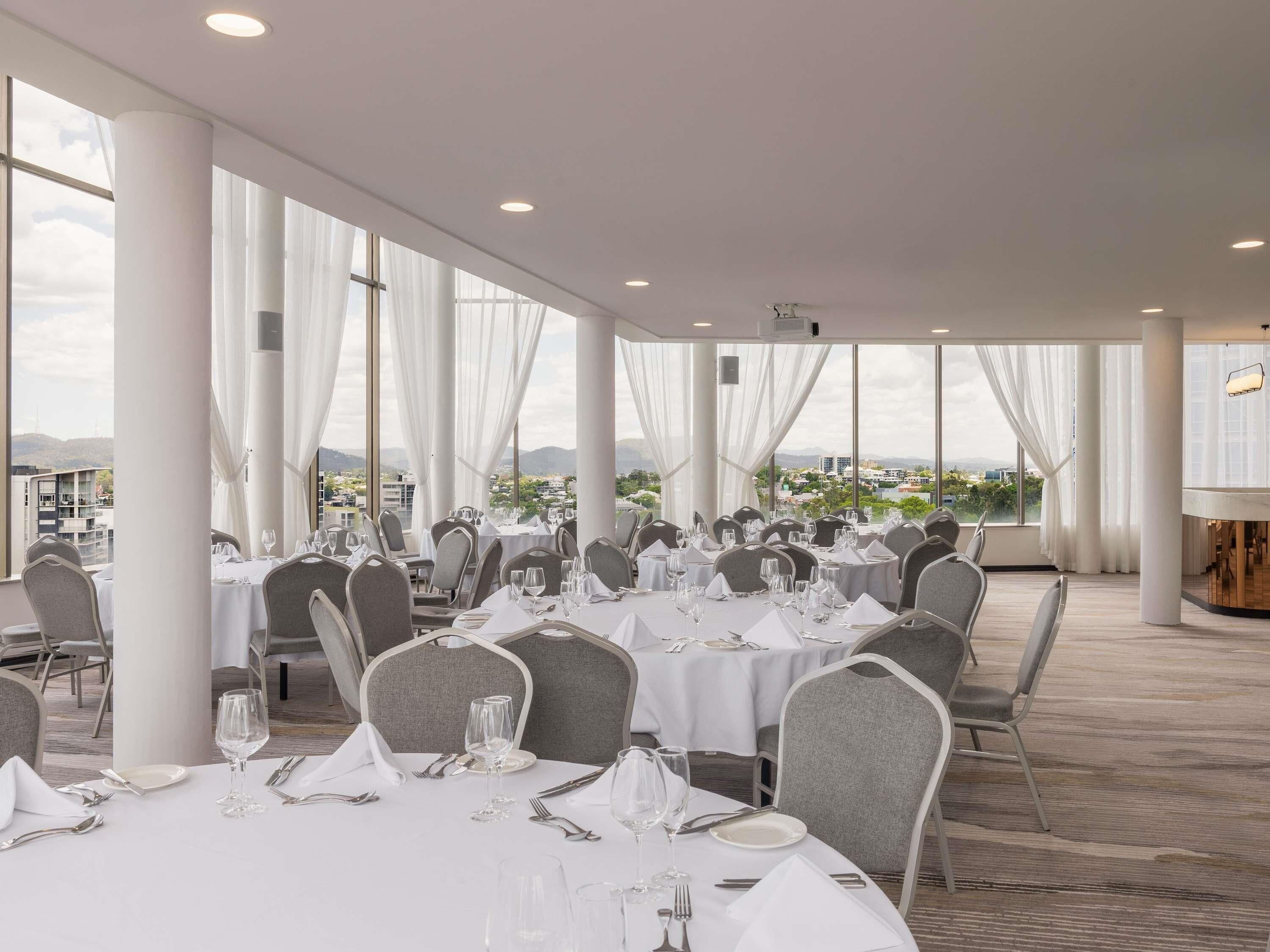 A spacious indoor dining area with round tables, white tablecloths, and grey chairs.
