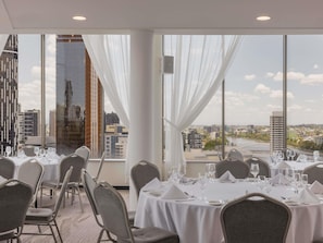 A dining area with tables set for service, large windows with curtains, and a city view. - Mercure Brisbane Spring Hill (Spring Hill)