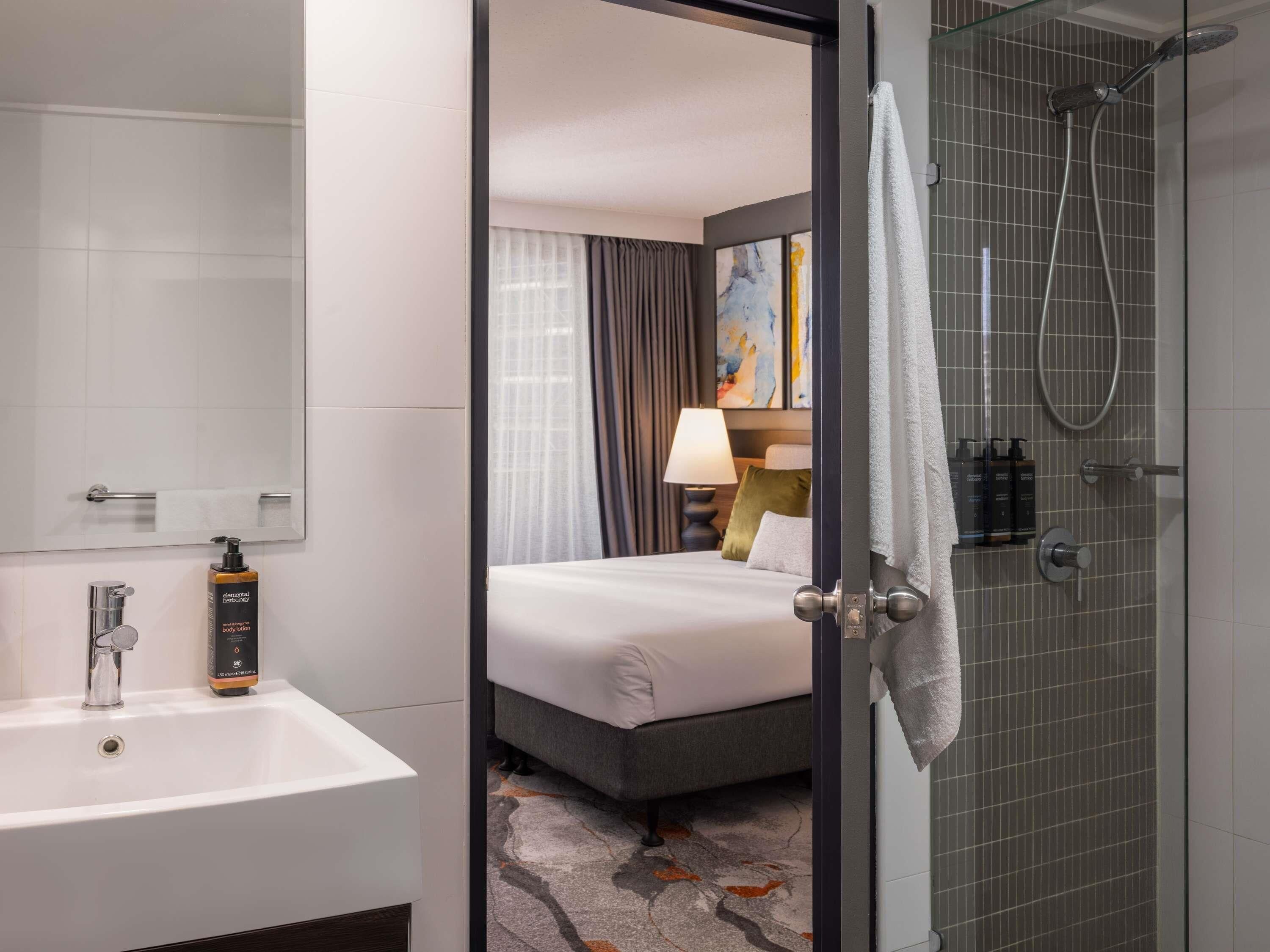 Een hotelkamer met een badkamer, een bed, een douche en een nachtkastje met een lamp.