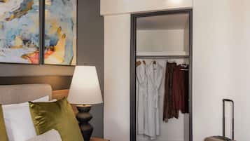 A hotel room with a bed, a bedside lamp, a wardrobe with hanging robes, and a suitcase.
