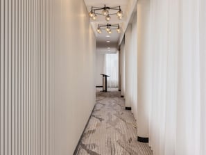 Pasillo de hotel con alfombra estampada, paredes blancas y un candelabro moderno.