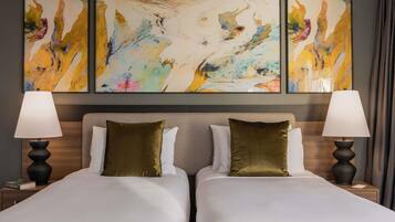 A hotel room with two beds, a large abstract painting above, and two bedside lamps.