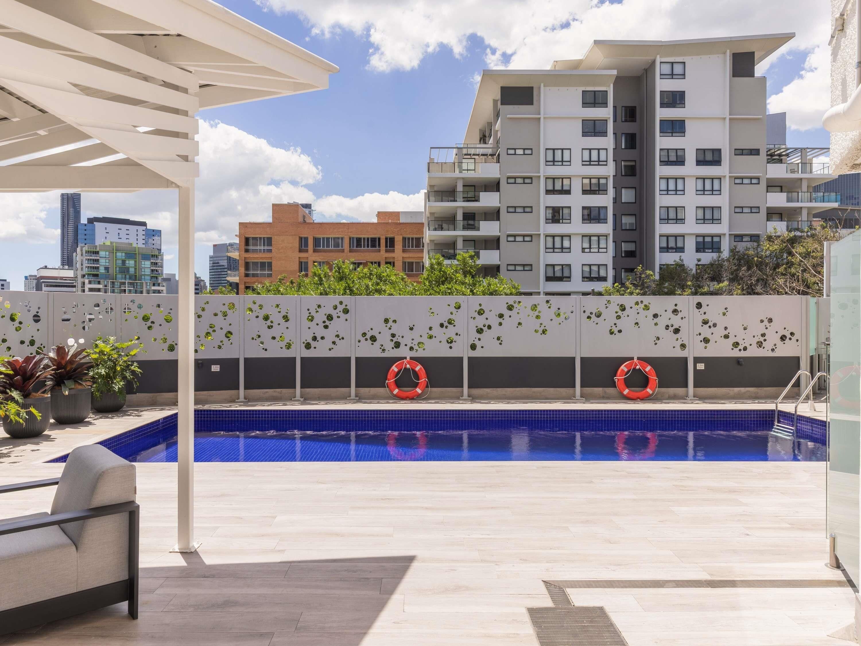 A rooftop pool with a pergola, a lifebuoy, and a view of surrounding buildings.