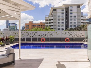 Una piscina en la azotea con una pérgola, un flotador salvavidas y vistas de edificios circundantes.