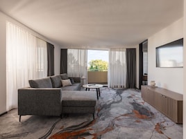 Une chambre d’hôtel moderne avec un canapé gris, une petite table ronde et une vue sur l’extérieur grâce à une porte coulissante.