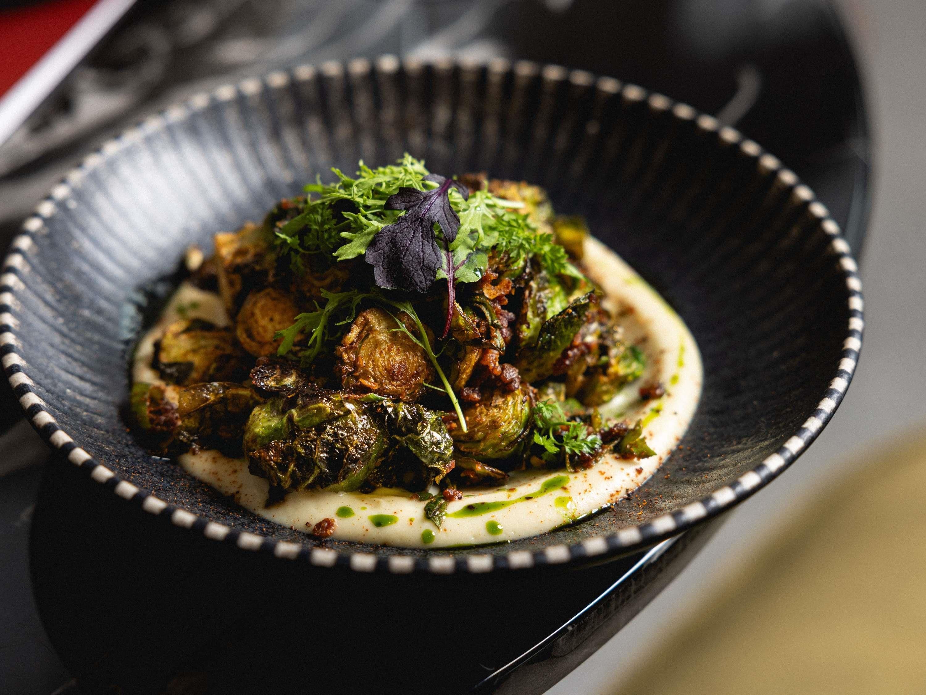 A dish with roasted Brussels sprouts and greens on a black plate.