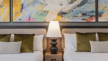 A hotel room with two beds, a nightstand with a lamp, and abstract art on the wall.