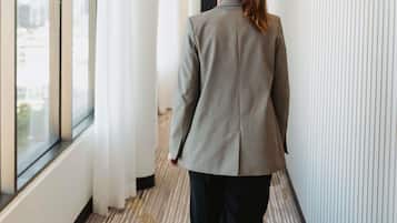 Una persona camina por un pasillo con una chaqueta de cuadros, una ventana a la izquierda y una alfombra estampada.