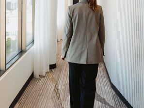 Una persona camina por un pasillo con una chaqueta de cuadros, una ventana a la izquierda y una alfombra estampada.