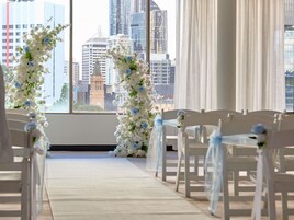 Pasillo con sillas blancas y decoración floral, que conduce a una ventana con vista panorámica de la ciudad.