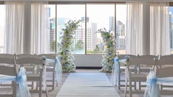 Preparação para cerimônia de casamento, com cadeiras brancas e um tapete branco no corredor, emoldurado por arcos florais.