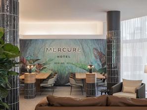 A modern hotel lobby with a mural, a wooden reception desk, and a seating area with a sofa and chairs. - Mercure Brisbane Spring Hill (Spring Hill)