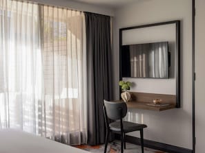 Habitación de hotel con un ventanal grande, una silla, una mesita con un florero y un televisor montado.