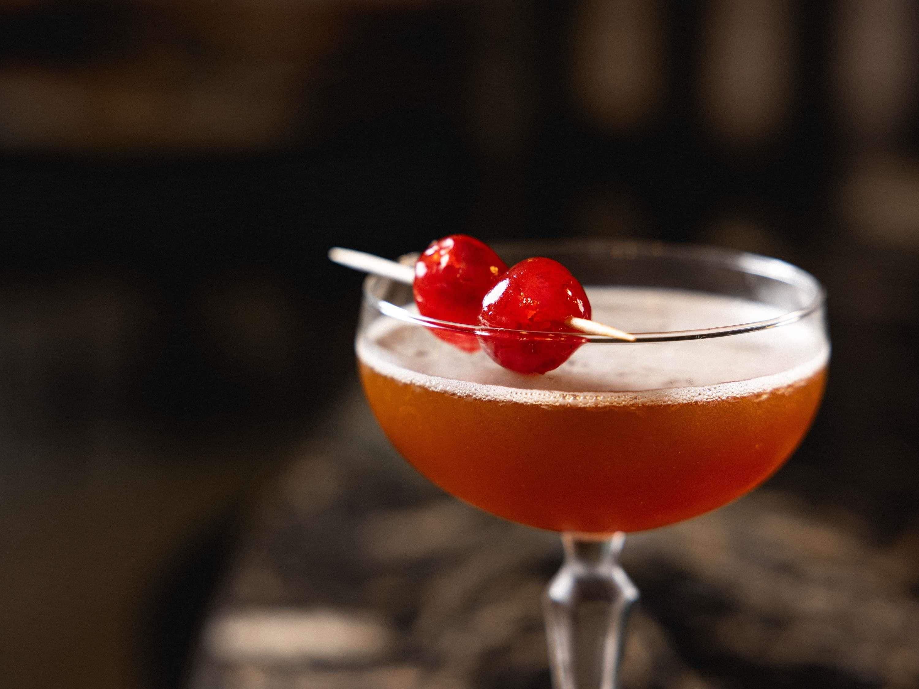 A cocktail in a stemmed glass with a cherry garnish.