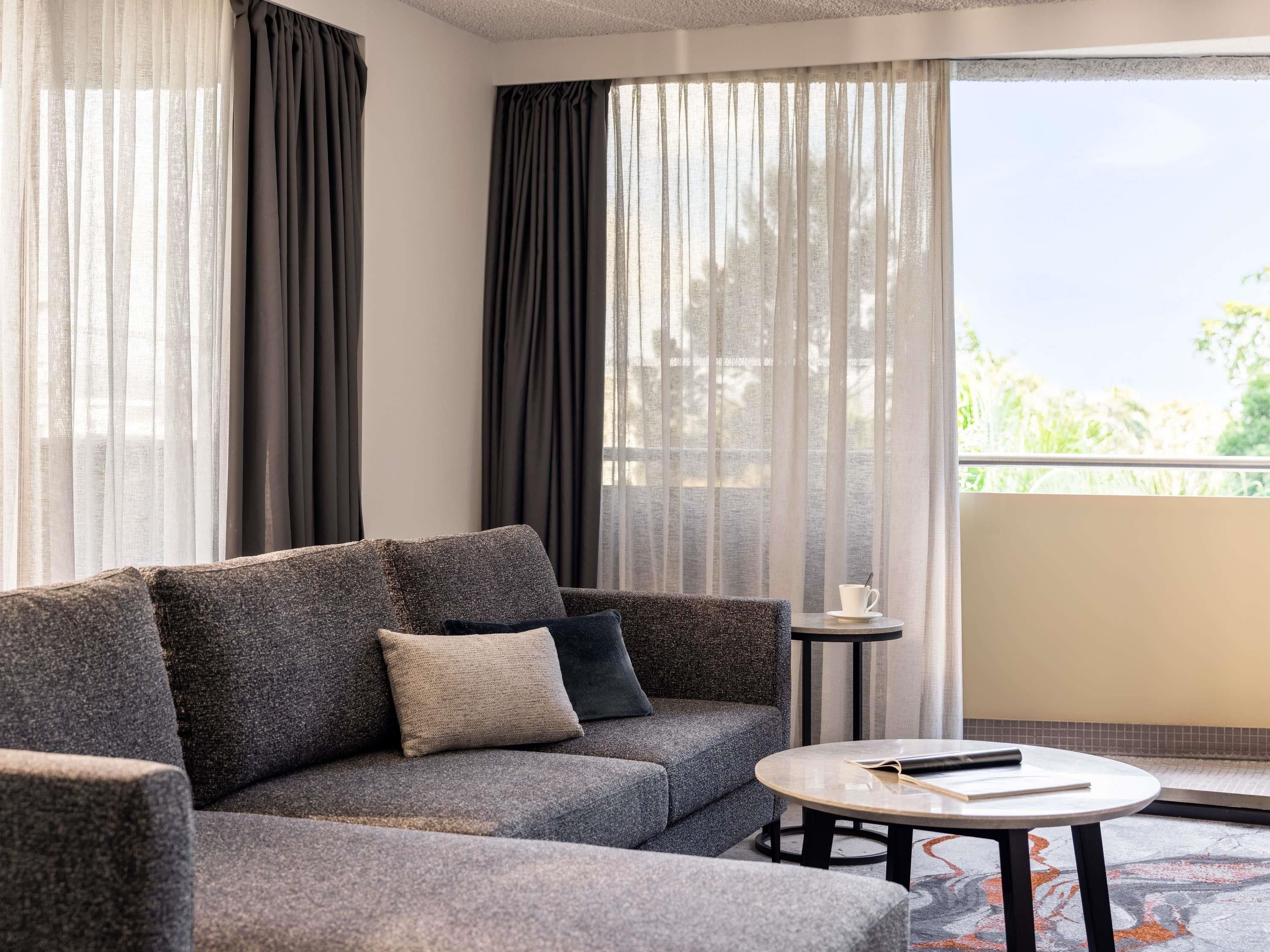 A modern living room with a grey sofa, a small round table, and sheer curtains.