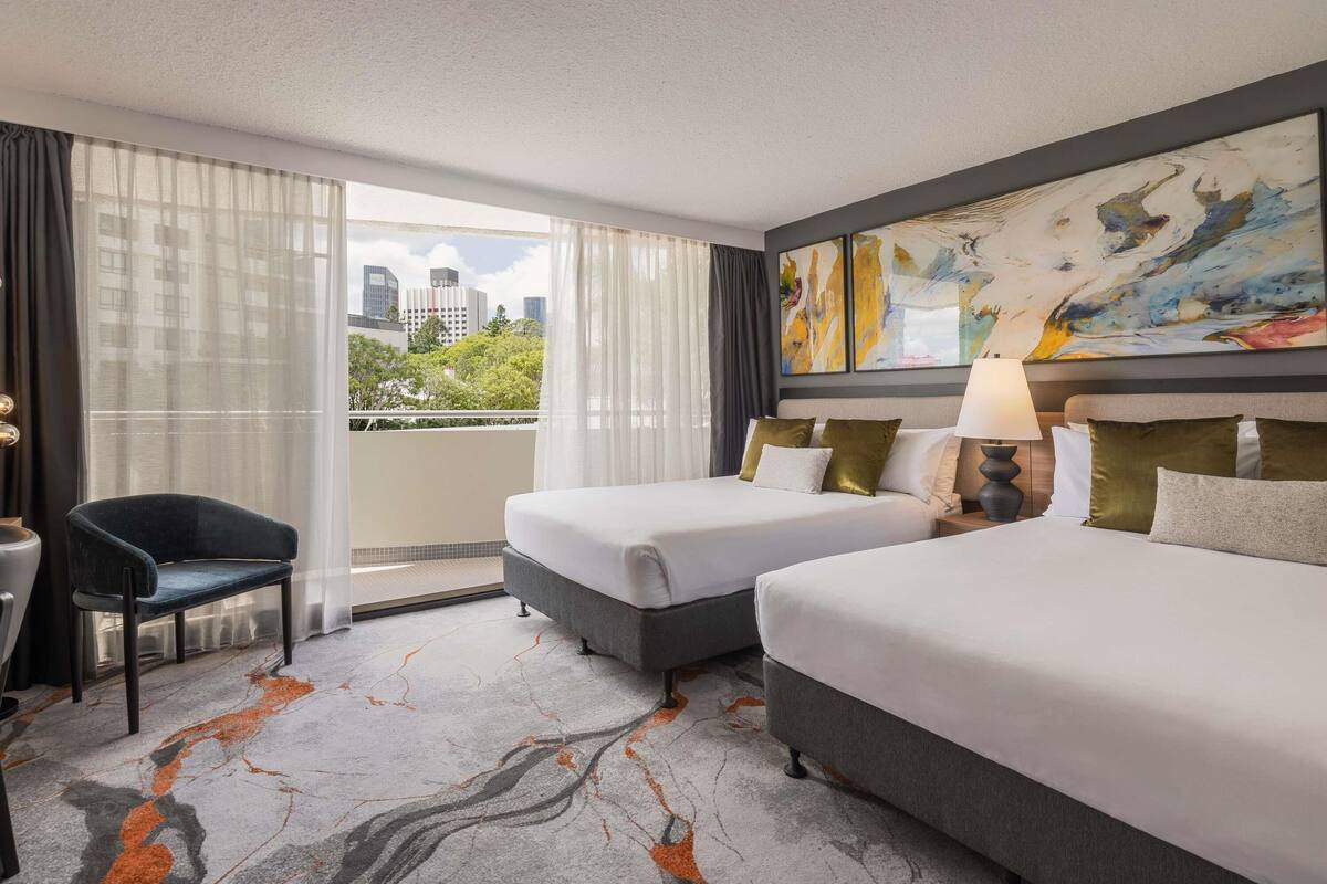 Habitación de hotel con dos camas, una silla, un escritorio, un cuadro y vistas a la ciudad.