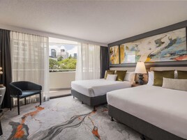 Hotelkamer met twee bedden, een stoel, een bureau, een schilderij en uitzicht op de stad.