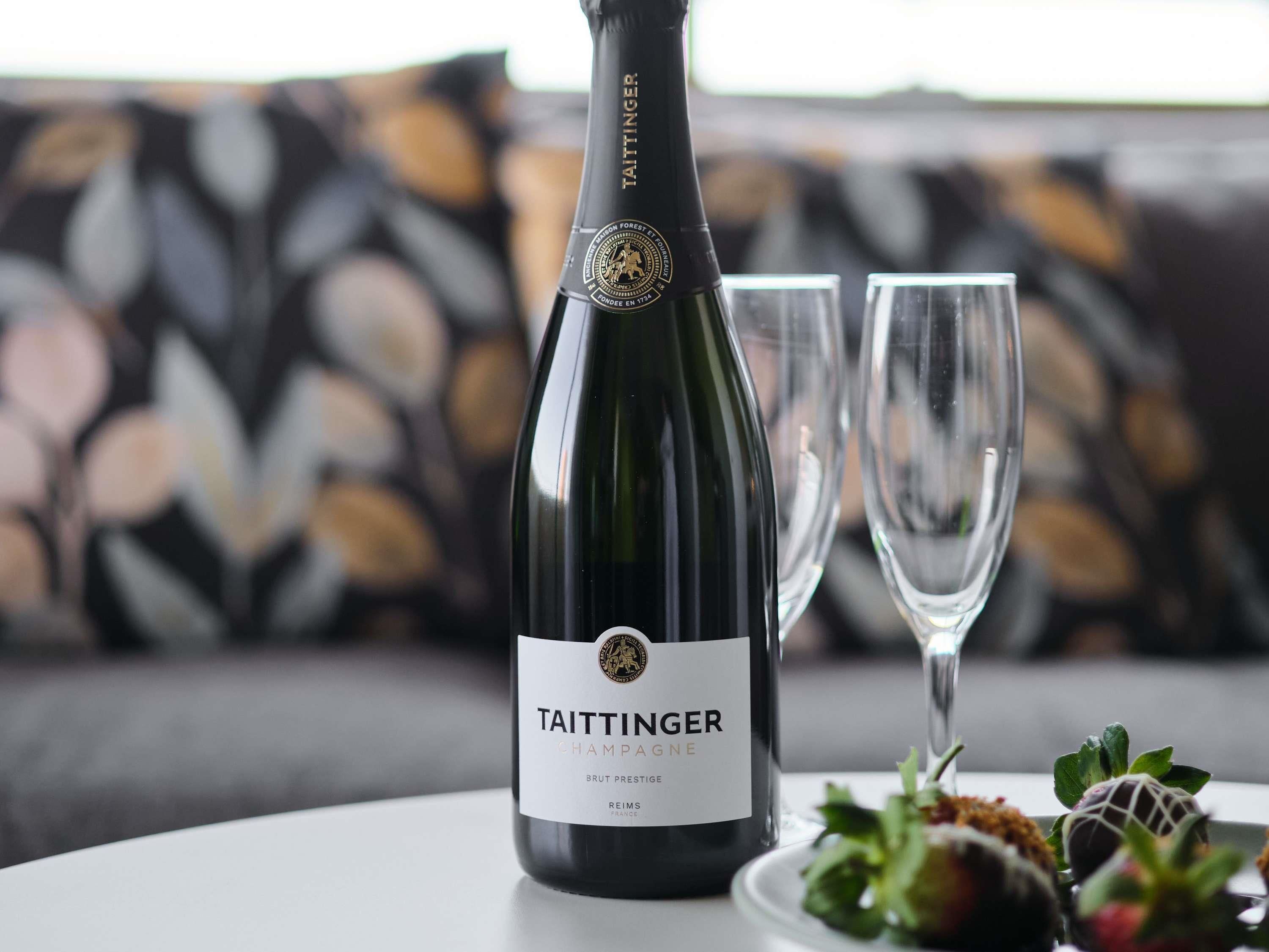 A bottle of Taittinger Champagne on a table with two empty glasses and a plate of strawberries.