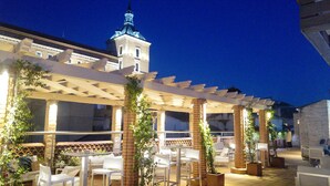 An outdoor patio area with white chairs and tables, brick pillars, and potted plants. - Hotel Carlos V (Toledo)