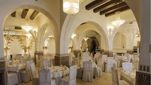A banquet hall with round tables, white chairs, and chandeliers. - Hotel Carlos V (Toledo)