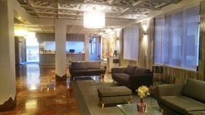 A spacious lobby with a polished wooden floor, multiple seating areas, and a reception desk in the background. - Hotel Carlos V (Toledo)