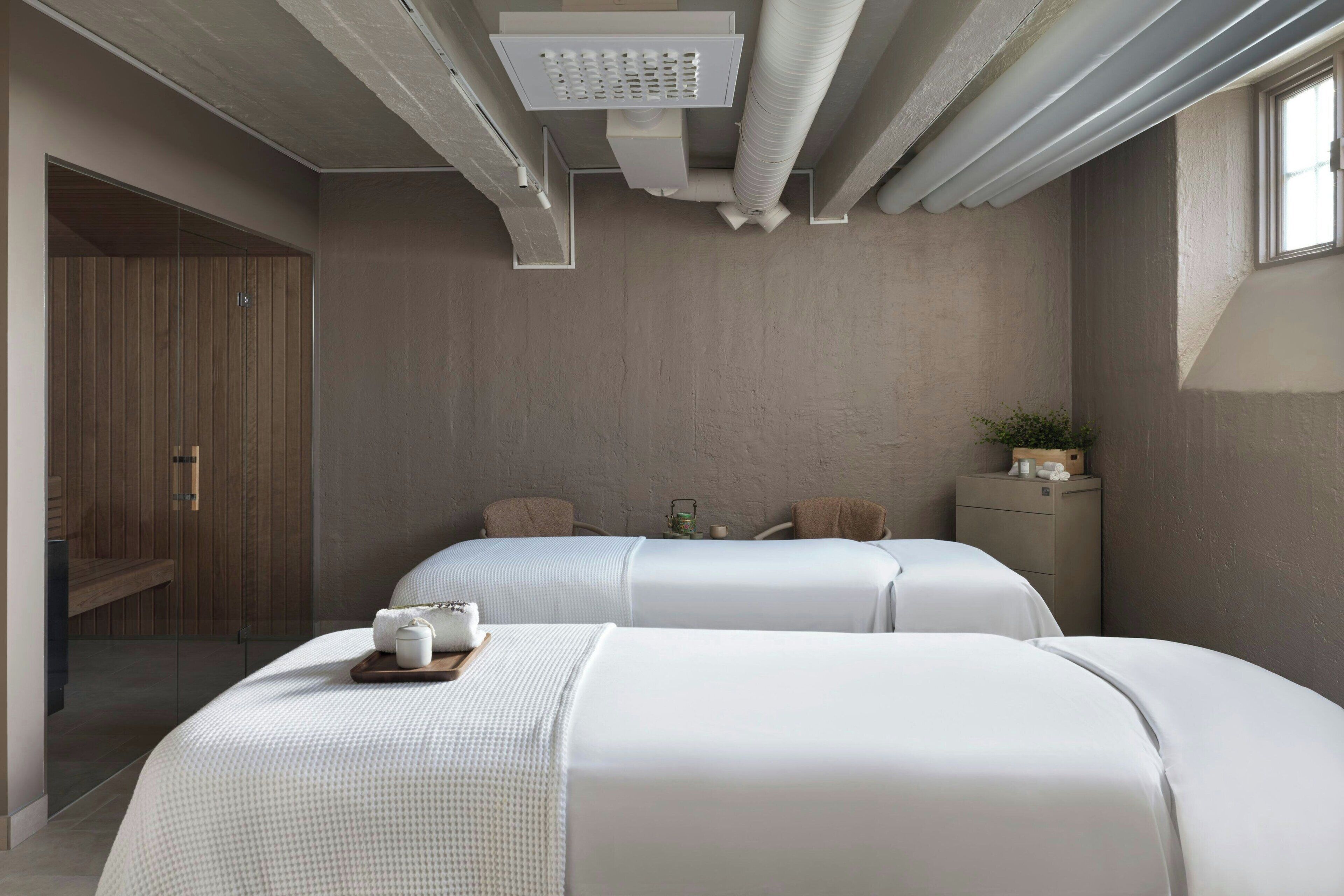 A modern bedroom with two beds, a wooden wardrobe, a small bedside table, and a window.