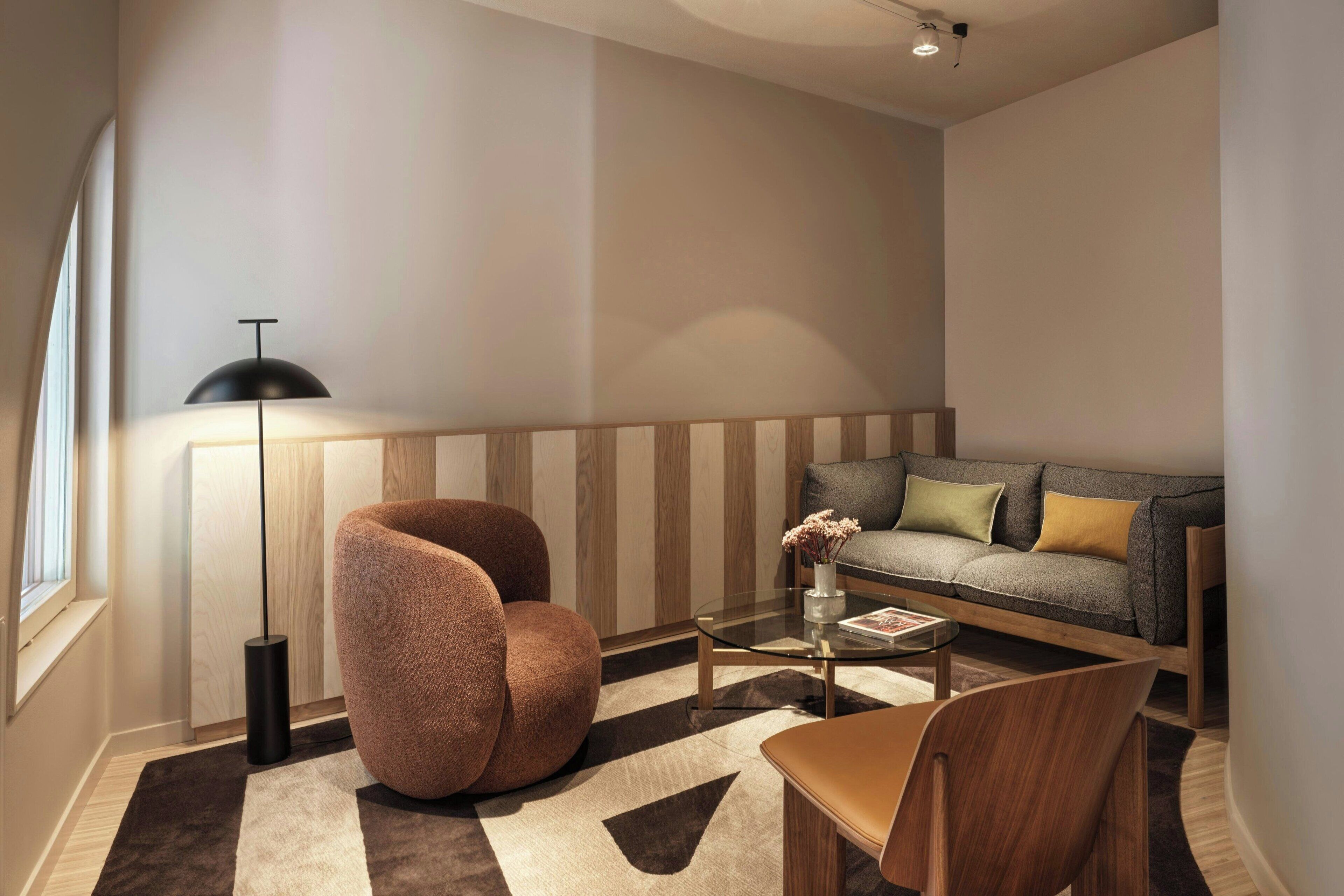 Una sala de estar moderna con un sillón redondo y texturizado, una mesa de centro de vidrio, un sofá con cojines y una lámpara de pie.