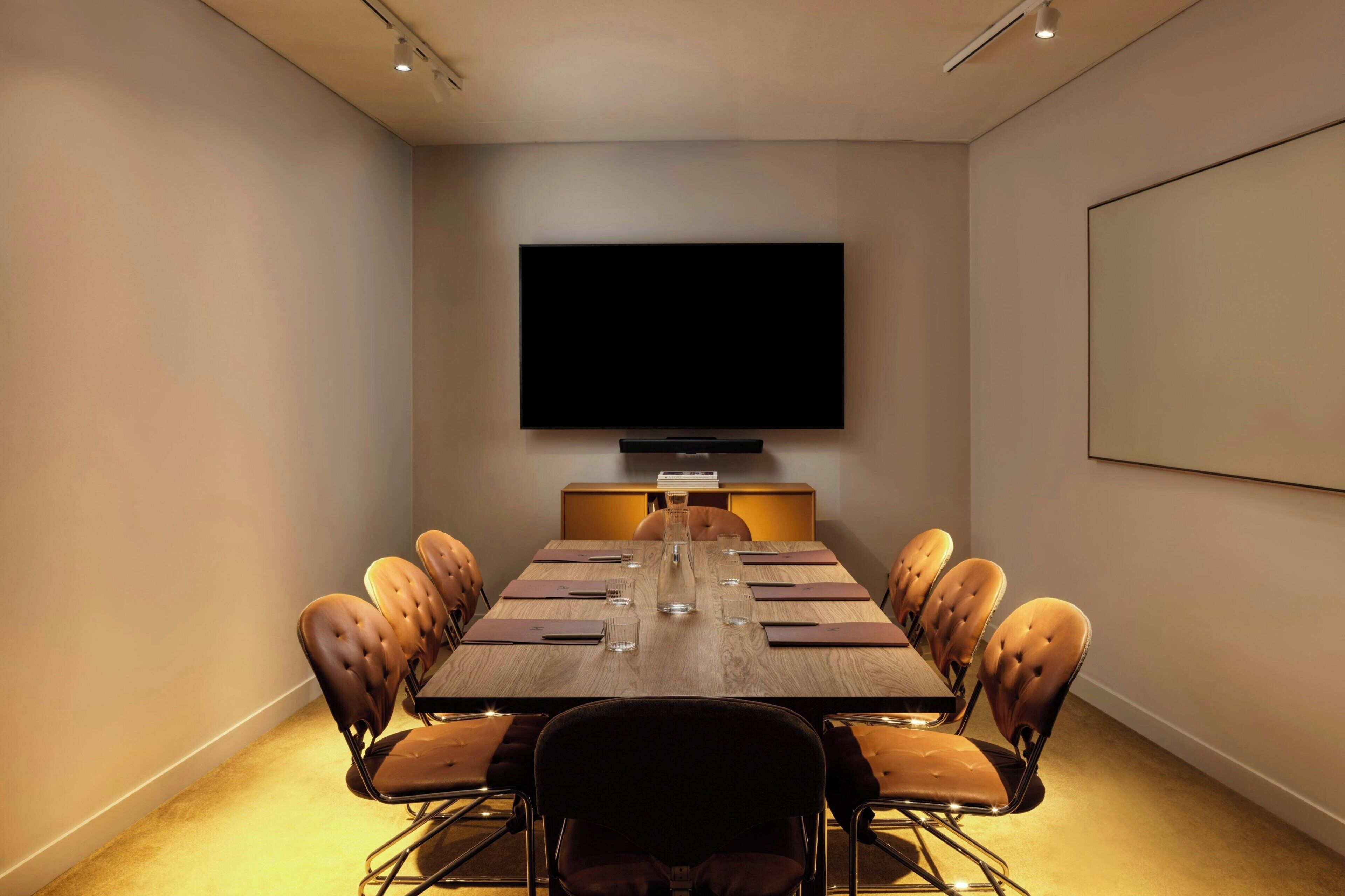 A conference room with a long table, chairs, a flat-screen TV, and a projector screen.