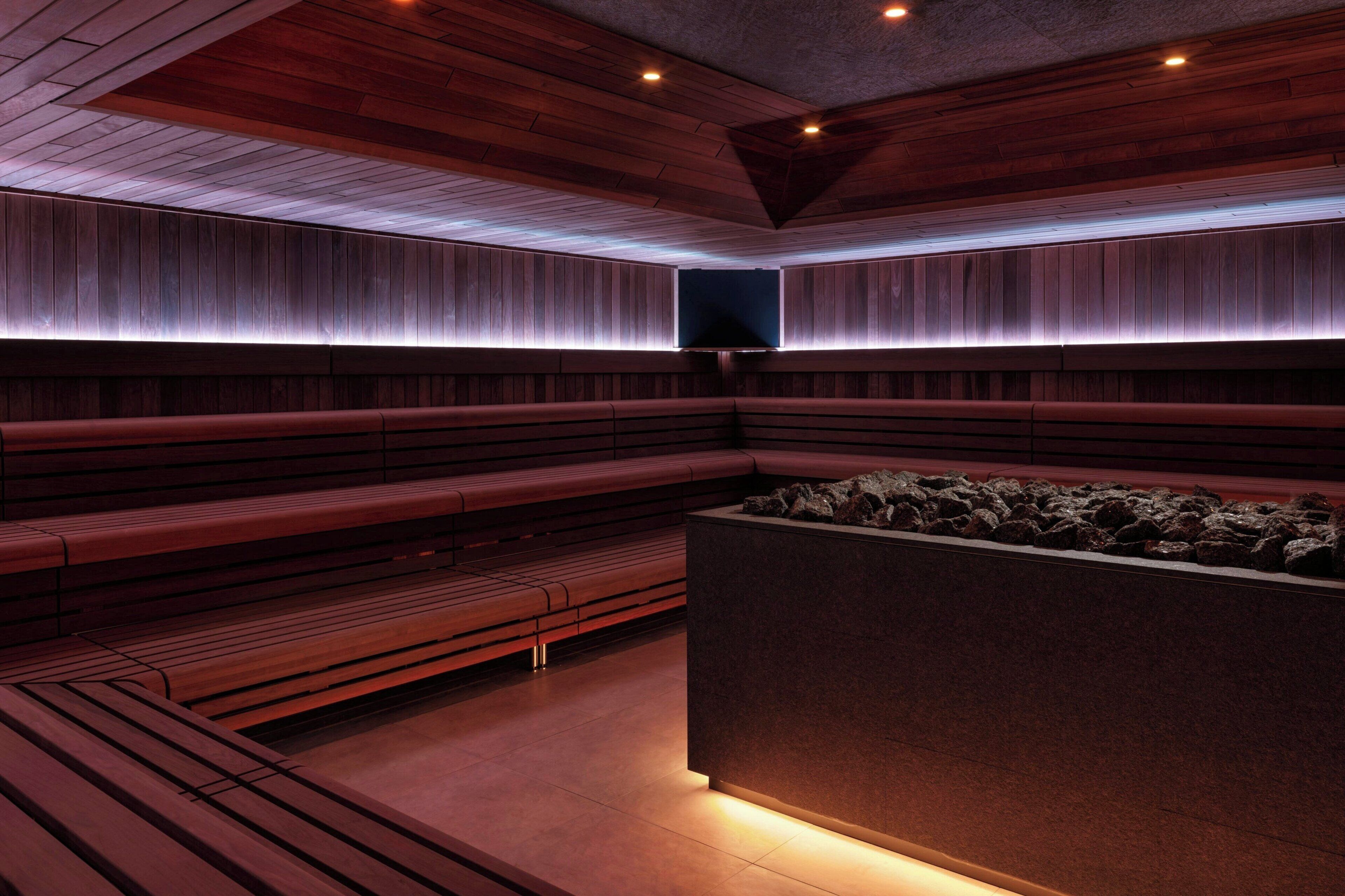 A modern sauna with wooden benches and a central heated stone area.