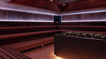 A modern sauna with wooden benches and a central heated stone area.