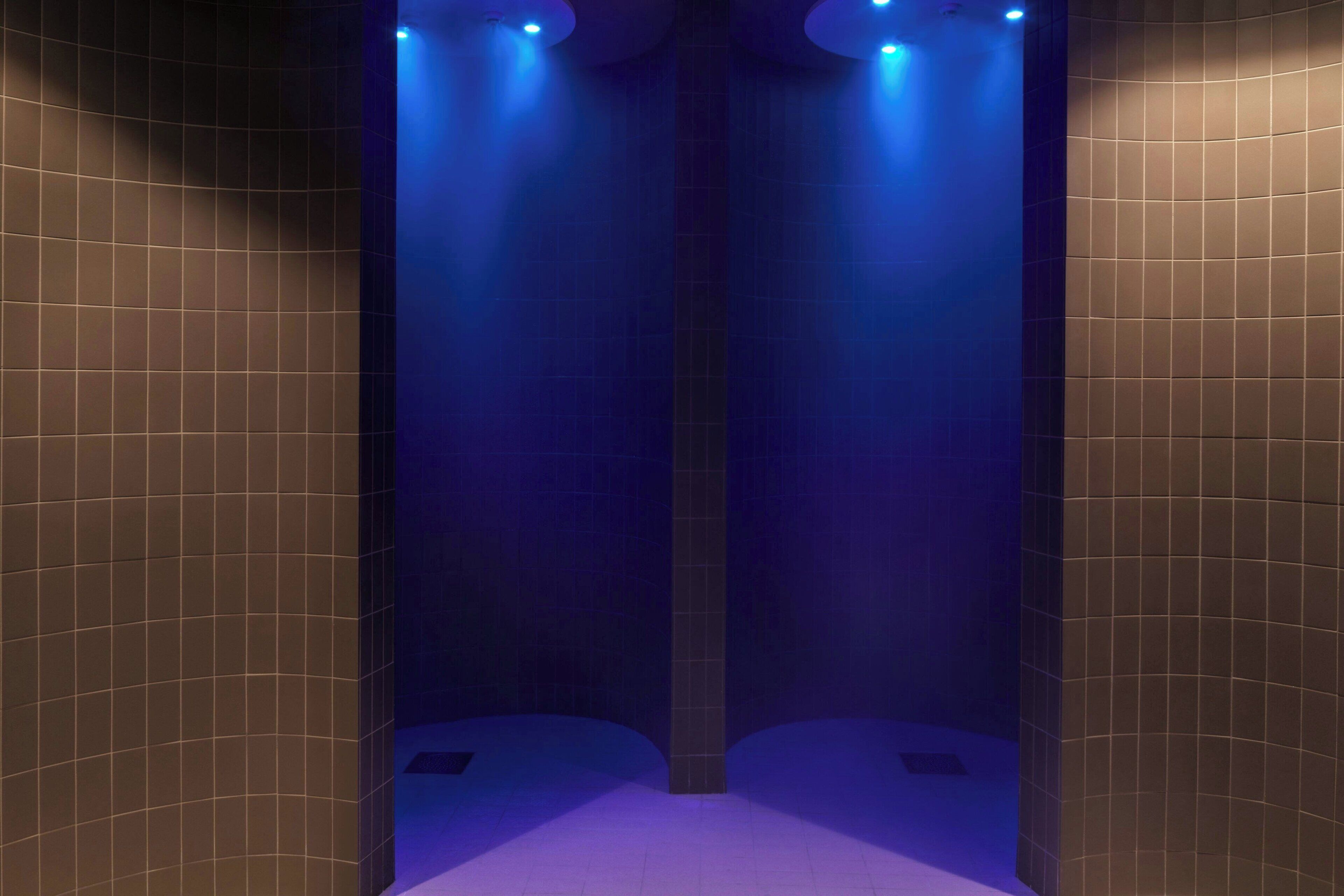 A narrow, tiled bathroom with blue lighting and a central column.