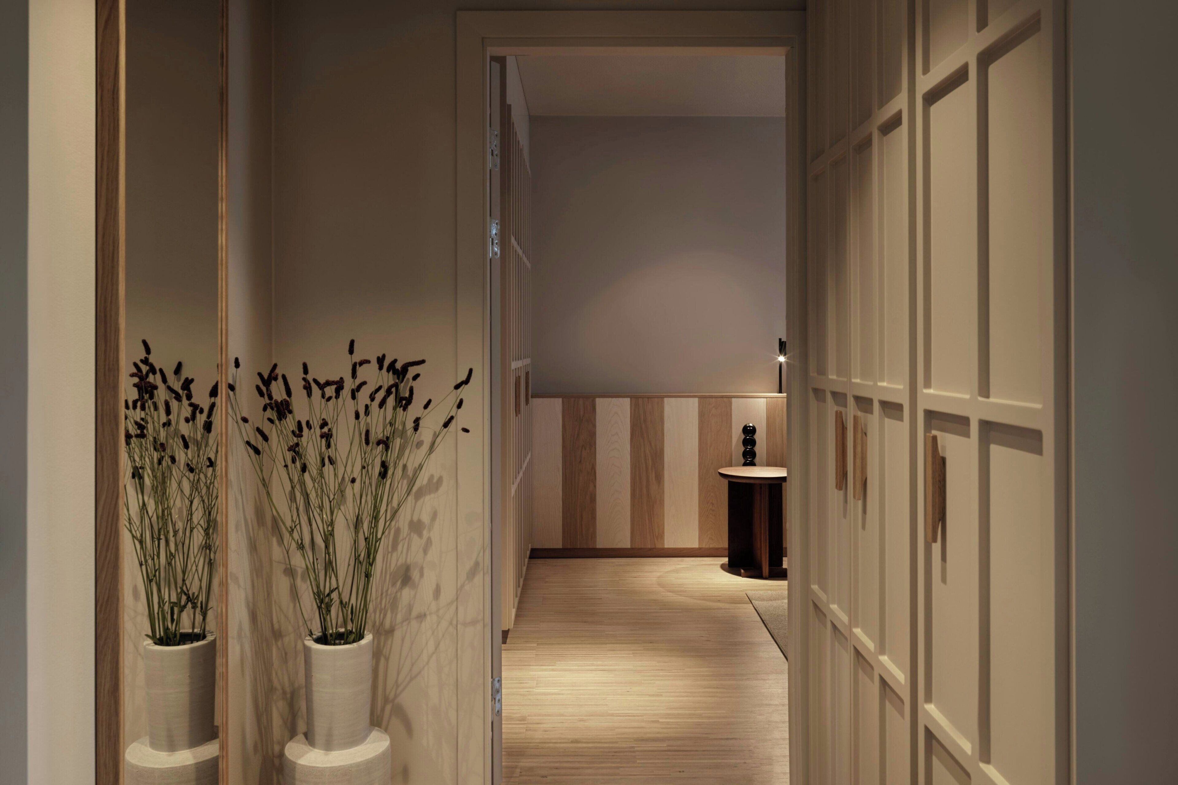 A narrow hallway with wooden flooring, a small round table, and two potted plants.