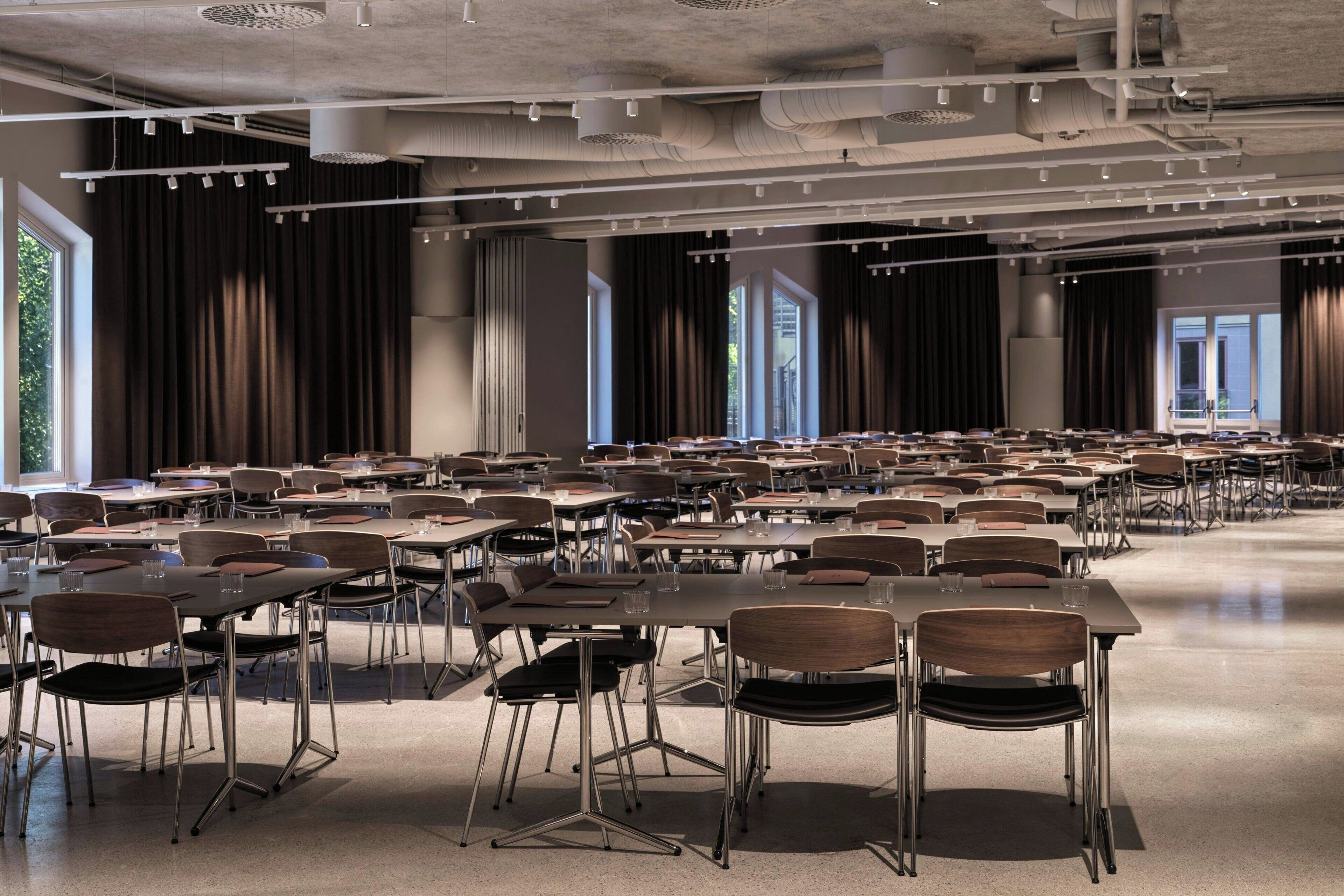 Un salón de conferencias amplio con filas de mesas y sillas, ventanas grandes y un diseño moderno en el techo.