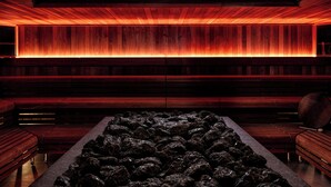 A dimly lit room with wooden benches and a central rock feature. - Hagastrand, Autograph Collection (Solna)