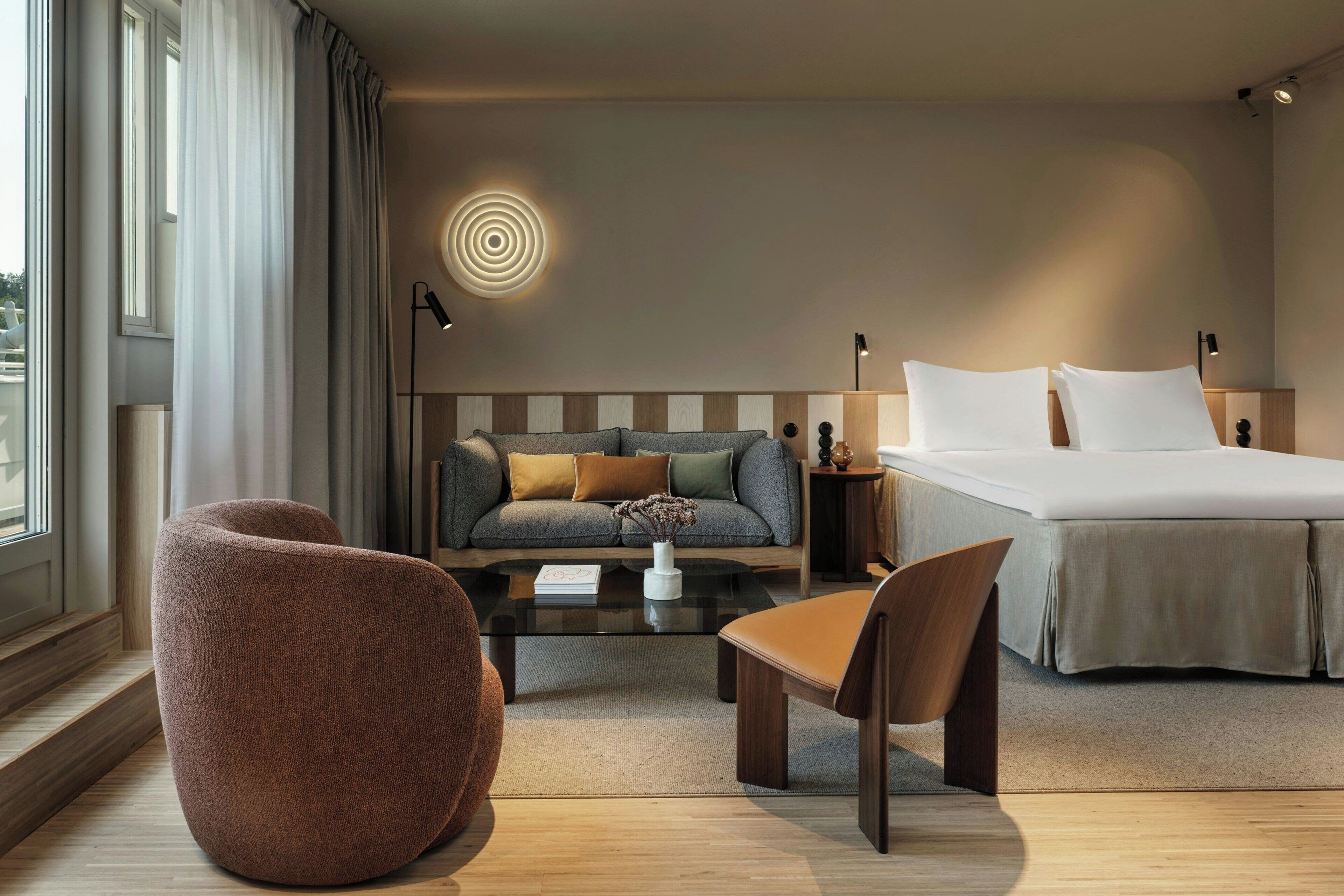 Ett modernt hotellrum med en stor säng, en soffa, ett soffbord och en stol.
