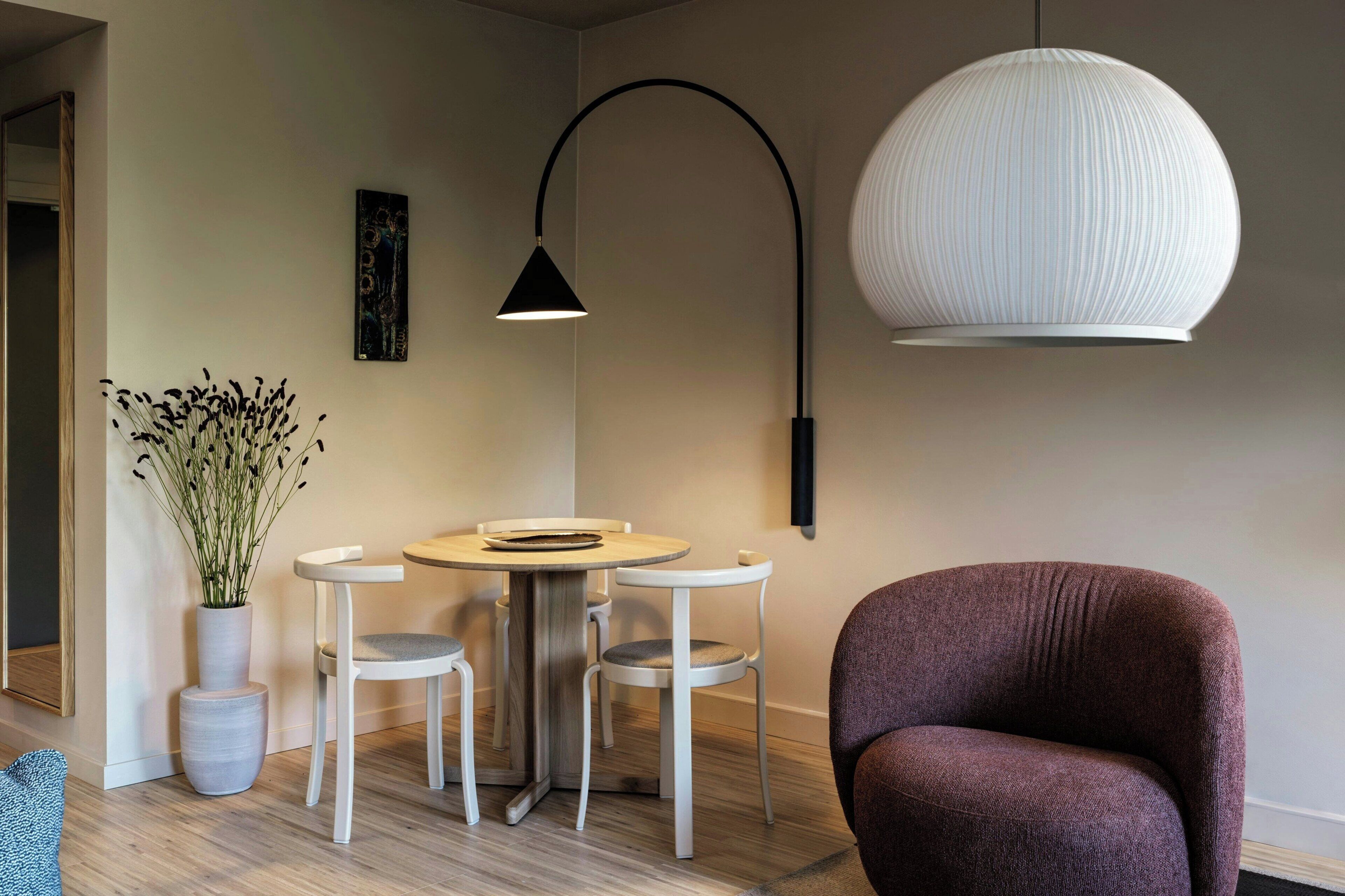 Un salon moderne avec une table ronde, quatre chaises, un grand lampadaire, un grand lustre et une plante en pot.