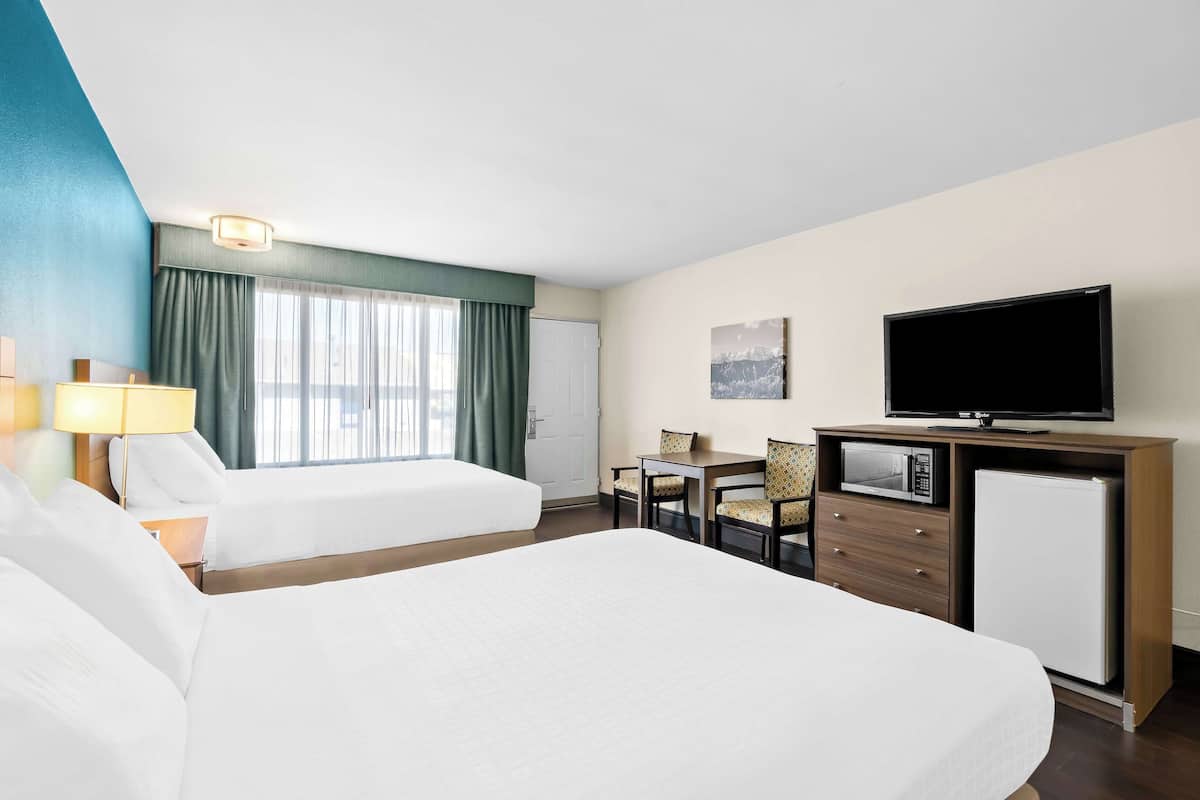 Une chambre d’hôtel avec deux lits, un bureau avec une chaise, une télévision, un four à micro-ondes et un réfrigérateur.