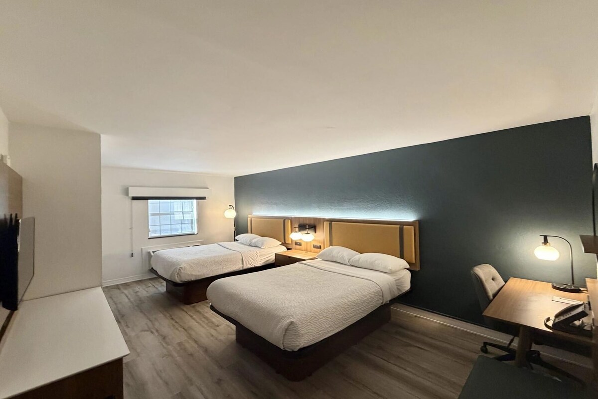 A hotel room with two beds, a desk, a chair, and a window.