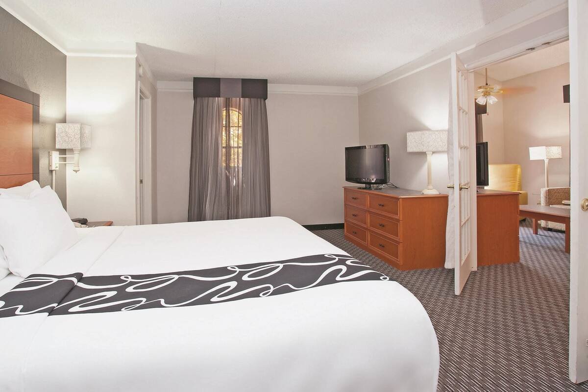 A hotel room with a large bed, a wooden dresser, a television, and a desk with a chair.