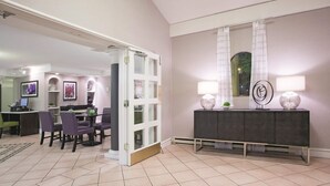 Un hall d’hôtel comprenant un espace repas, un comptoir d’accueil et un grand miroir agrémenté de deux lampes.