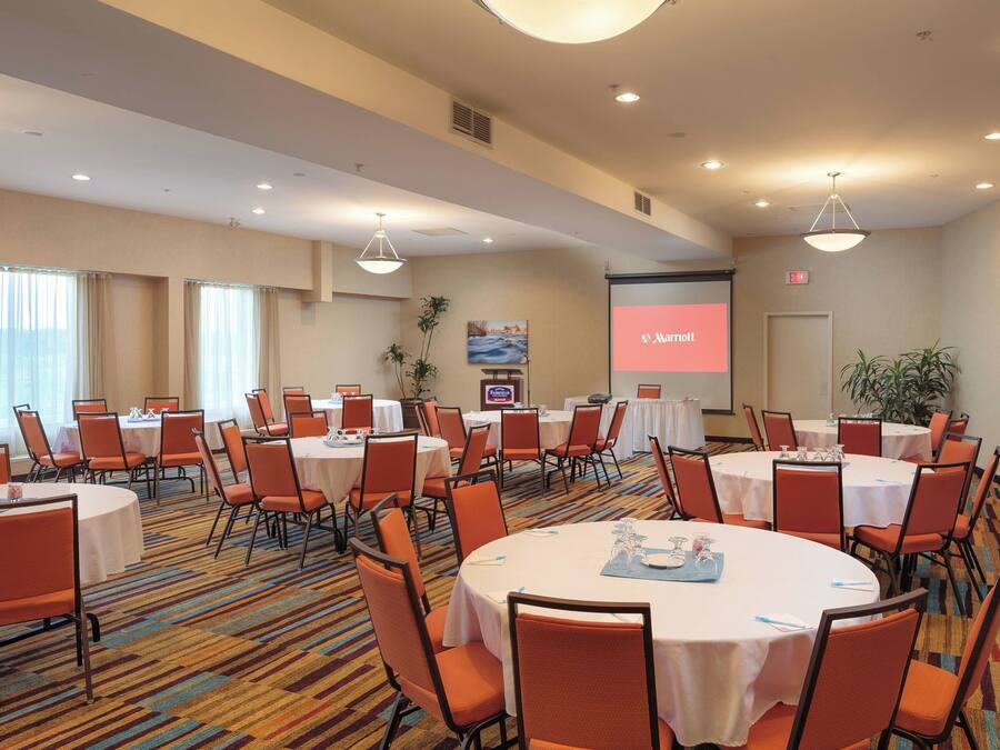 A conference room with multiple round tables and orange chairs, equipped with nameplates and water glasses.