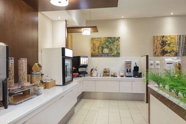A modern kitchen with white cabinets, a coffee station, and a painting of a forest.