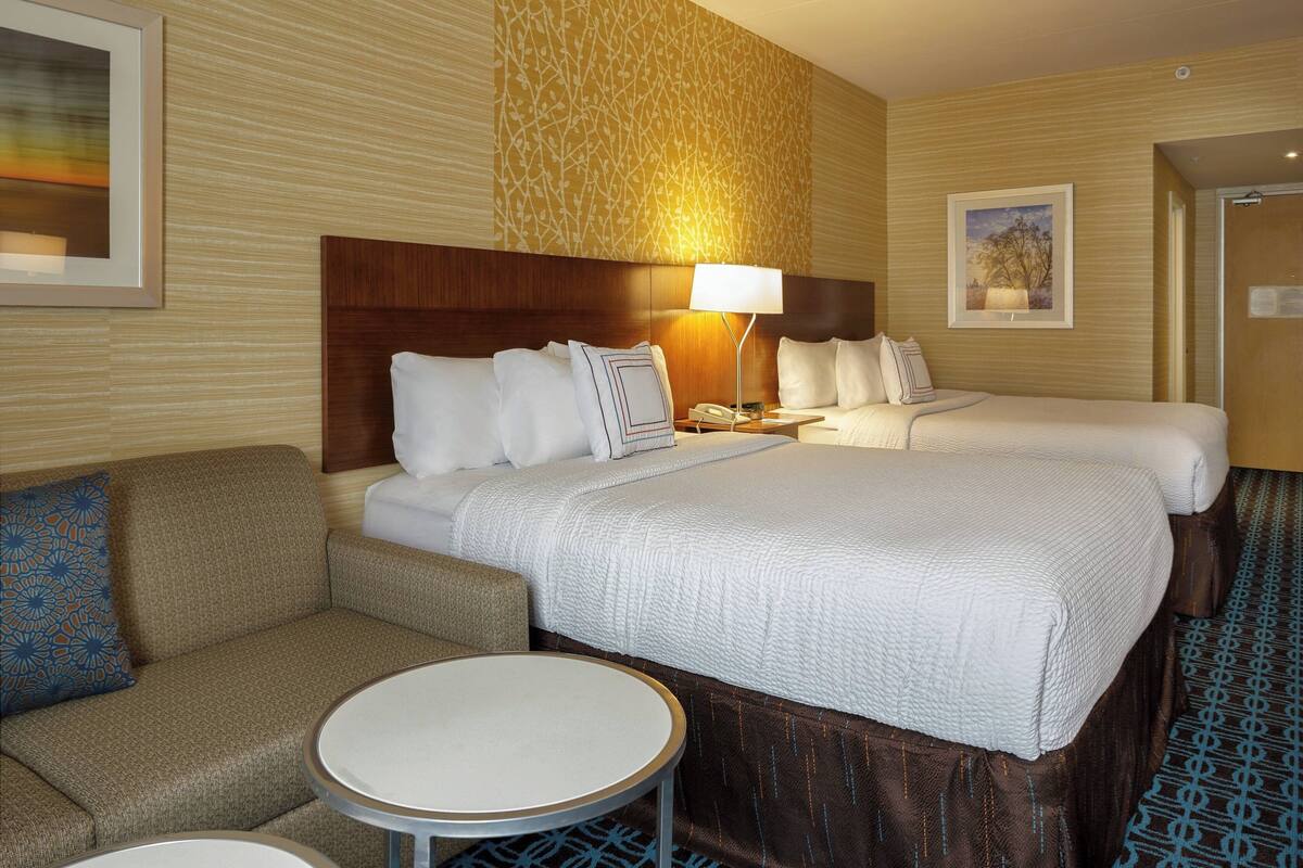 A hotel room with two beds, a sofa, a round table, and a patterned carpet.