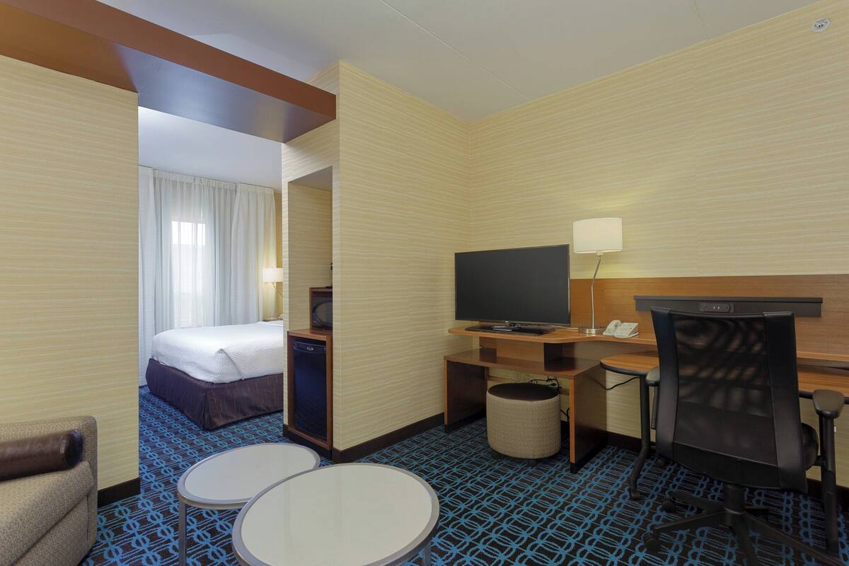 A hotel room with a bed, a desk with a computer, a TV, and two small tables.
