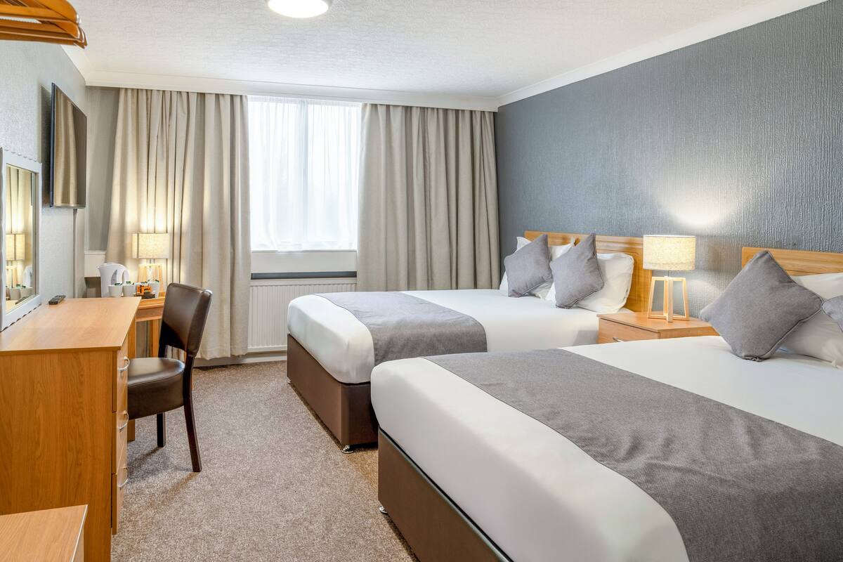A hotel room with two beds, a desk, a chair, and a window with curtains.