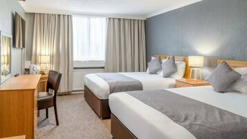 Habitación de hotel con dos camas, un escritorio, una silla y una ventana con cortinas.